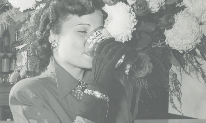 Black and white vintage photo of woman drinking out of a Sazerac glass